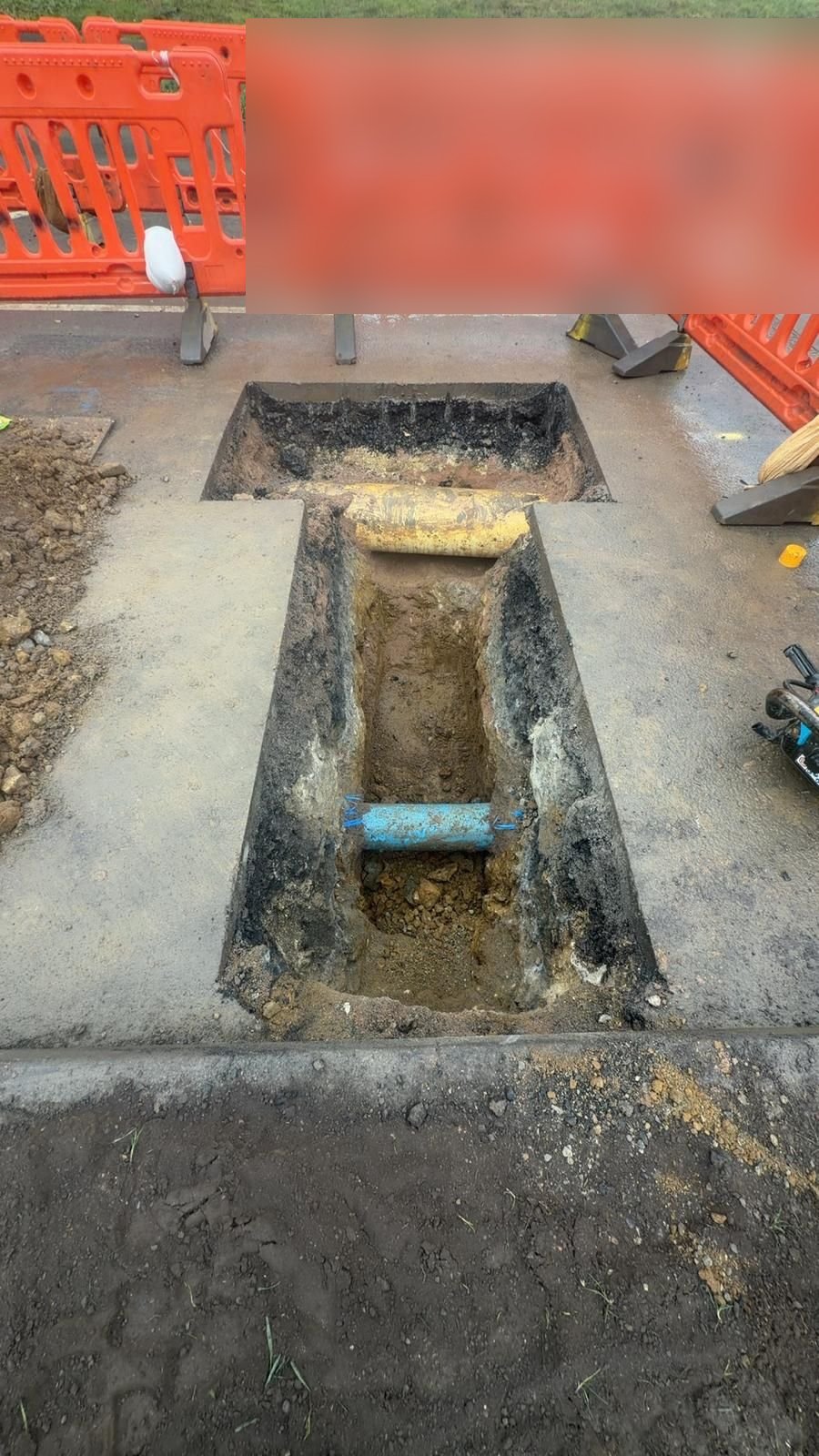 Excavation inside safety barriers exposing a yellow gas main and a blue pipe at the start of a CSEP gas mains connection