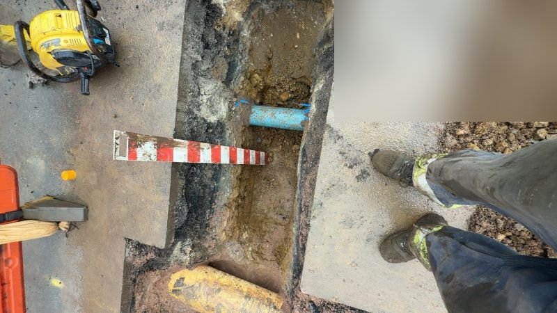 Open trench with a measuring pole across it, showing exposed yellow gas main and blue pipework during CSEP connection works
